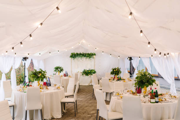 elegant white event space setup for wedding reception or corporate gathering under a tented ceiling with round tables and string lights