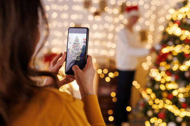 Woman taking picture of Christmas tree with smartphone.