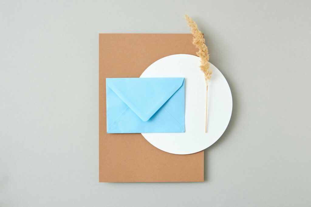 Envelope on top of a brown paper and a white circular placemat with dried grass.